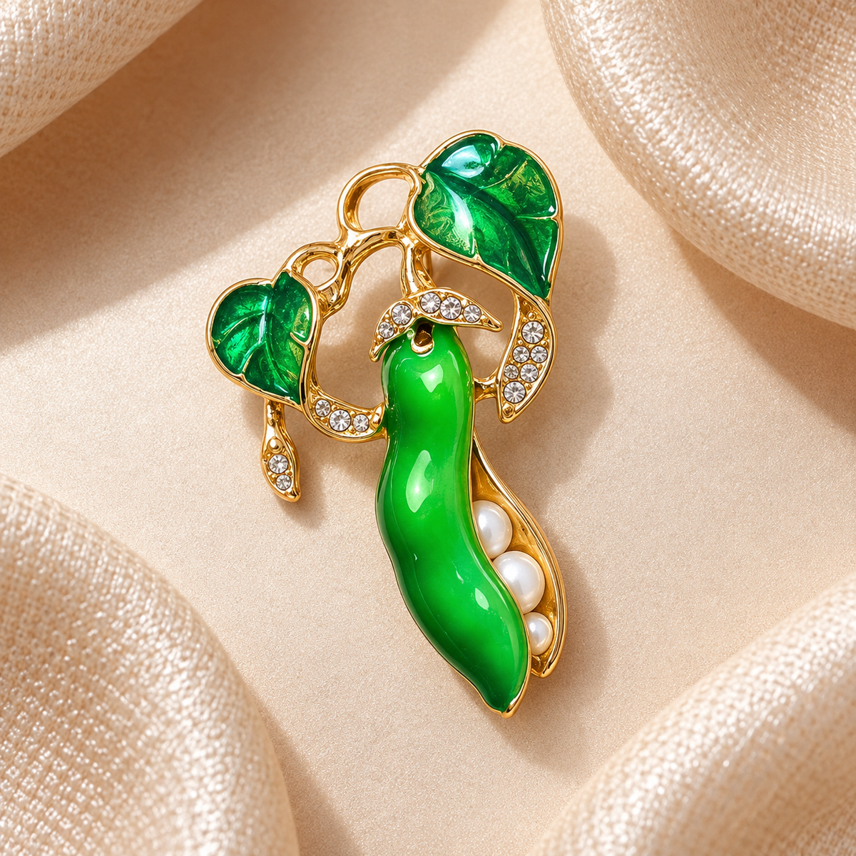Broche haricot magique vert émeraude et doré avec perles et strass sur fond carré en satin champagne