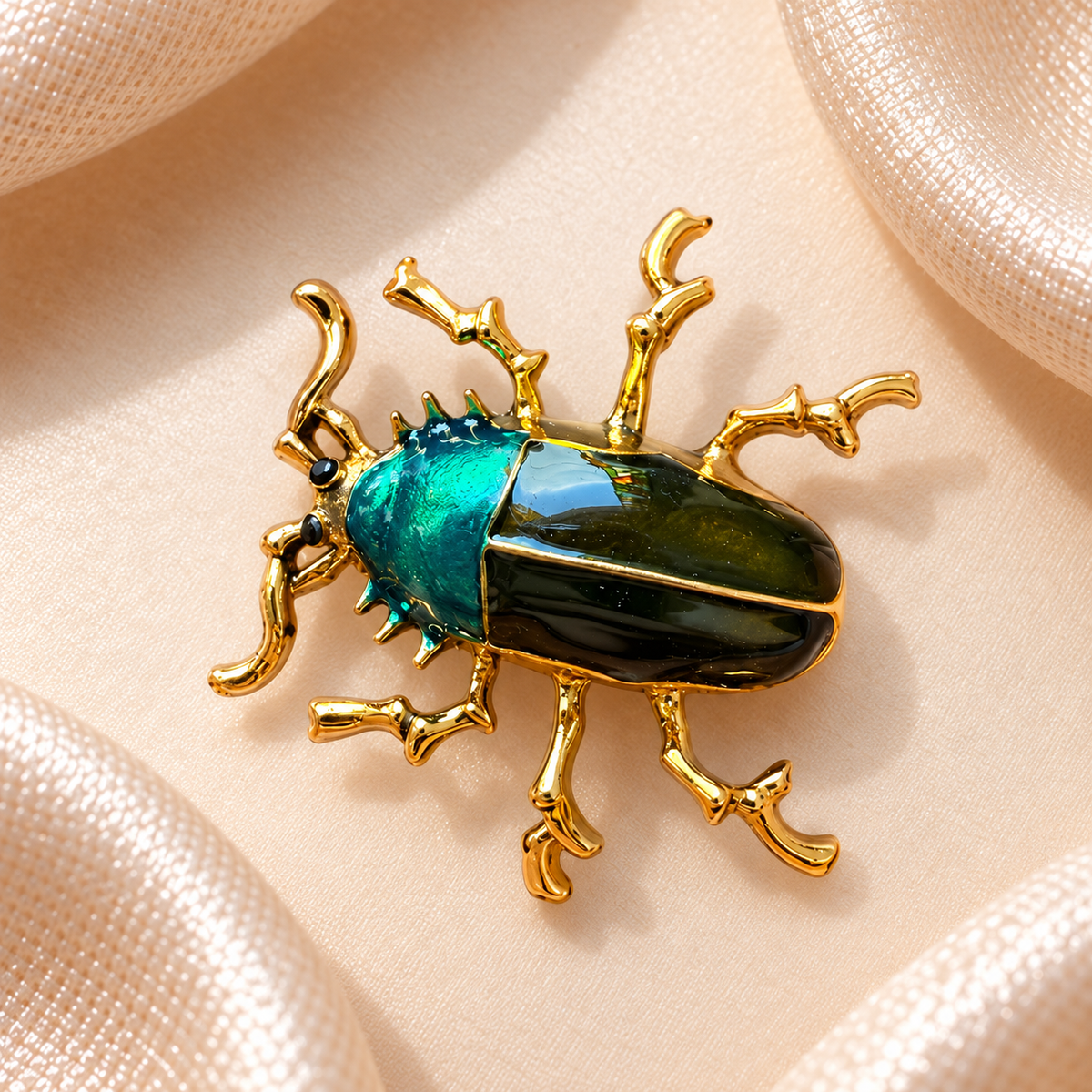 Broche scarabée doré avec détails émaillés turquoise et vert foncé sur fond satin champagne-beige