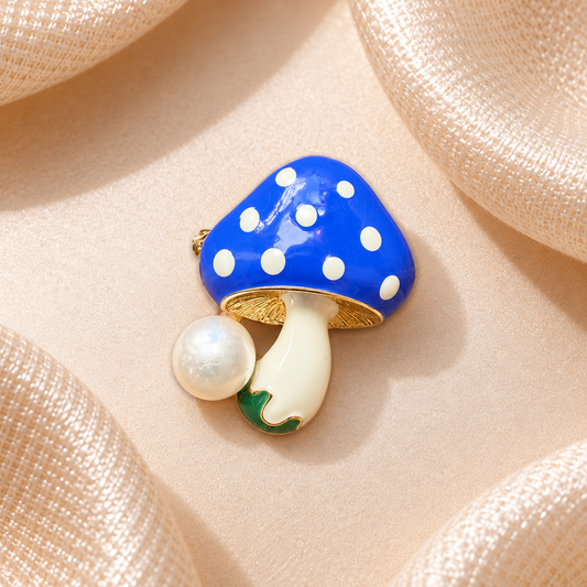 Broche champignon bleu à pois blancs avec tige ivoire, détails dorés et pendentif perle sur fond champagne satiné
