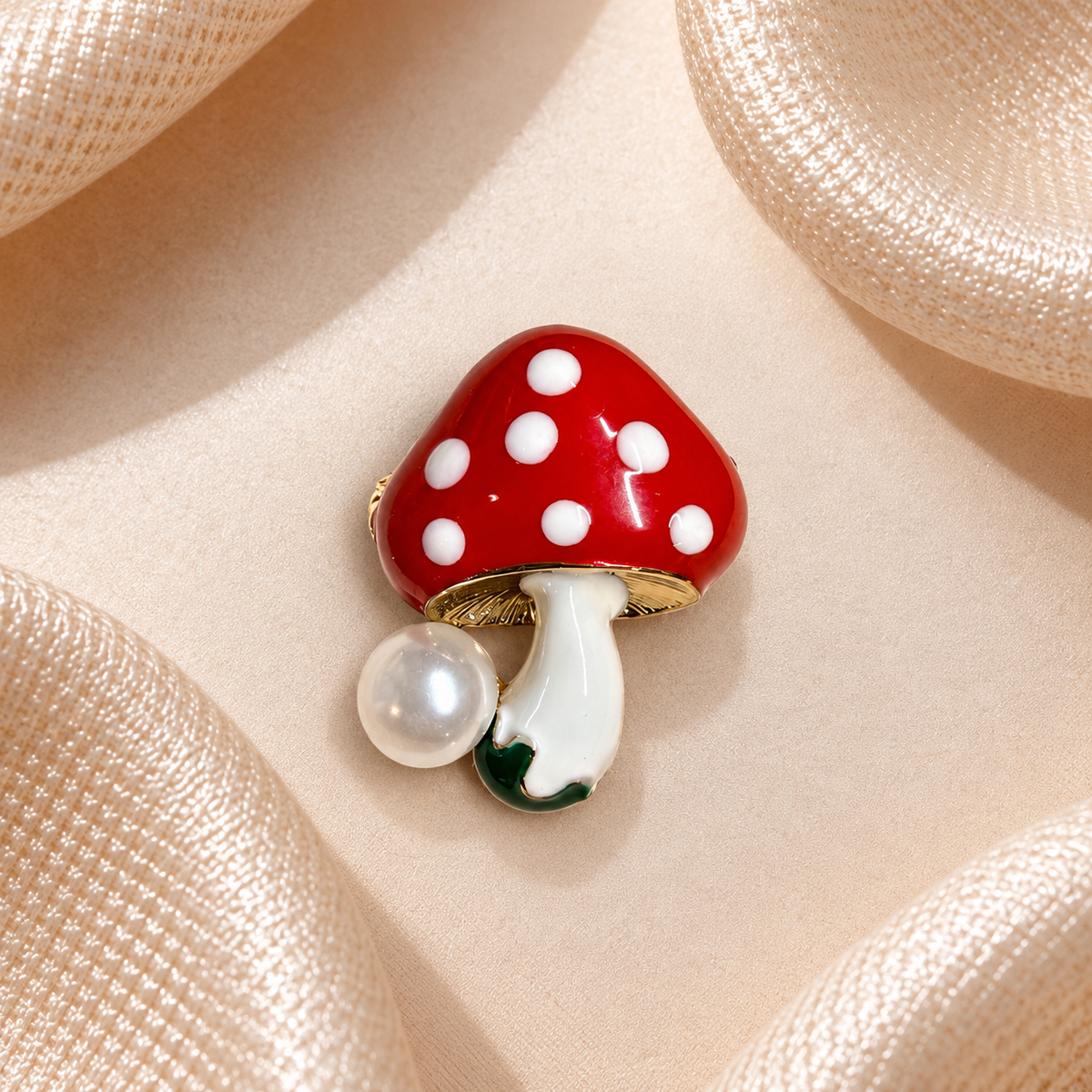 Broche champignon rouge à pois blancs, pied blanc, perle nacrée sur fond carré en satin champagne