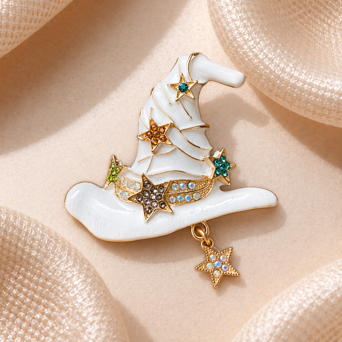 Broche chapeau de sorcière blanc nacré bordé d’or, décoré d’étoiles et de strass multicolores sur fond champagne satiné