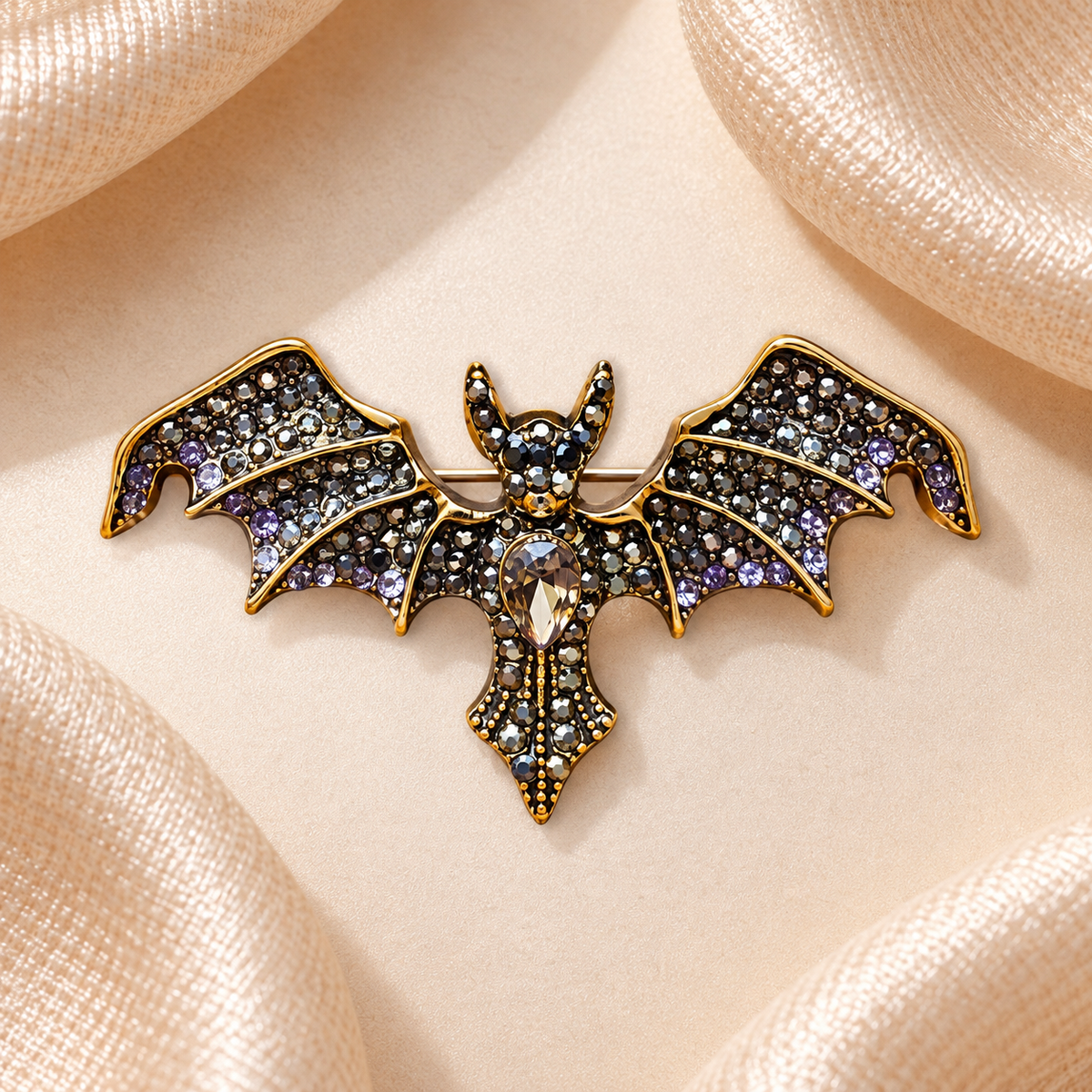 Broche chauve-souris dorée aux strass noirs, gris, argentés et violets sur fond satin champagne-beige