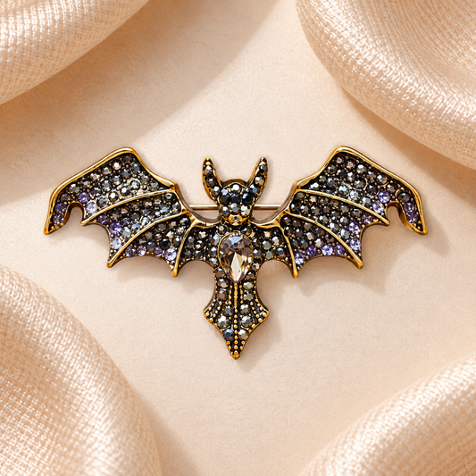 Broche chauve-souris dorée aux strass noirs, gris, argentés et violets sur fond satin champagne-beige