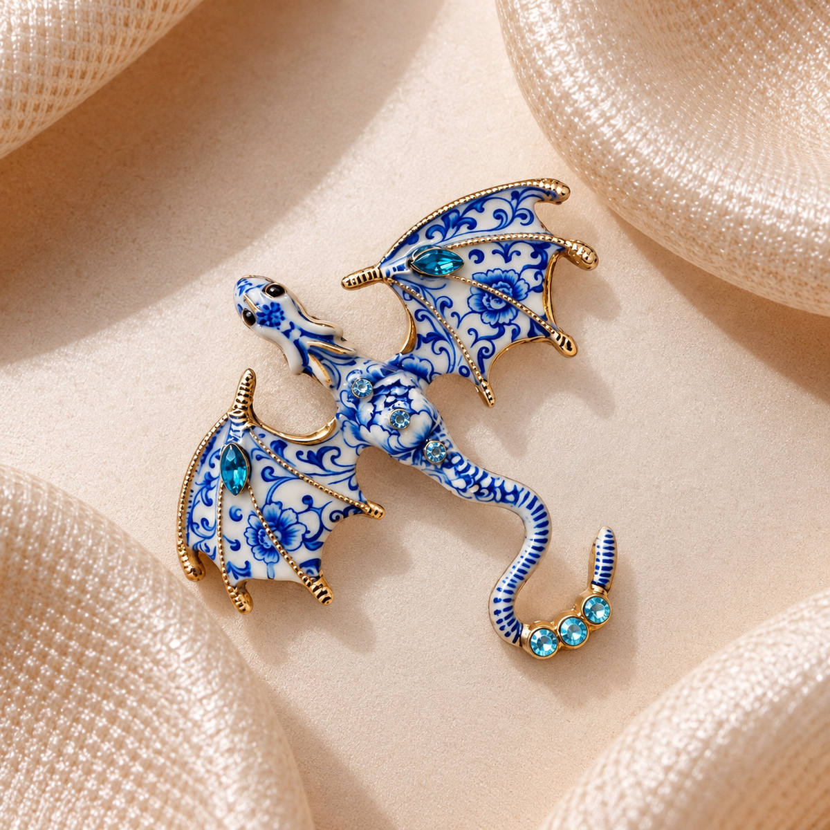 Broche dragon bleu et blanc à motifs floraux, détails dorés et cristaux turquoise sur tissu champagne satiné