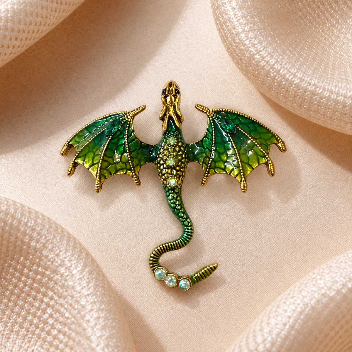 Broche dragon vert émeraude et doré intégrée sur fond de tissu champagne satiné, ailes déployées