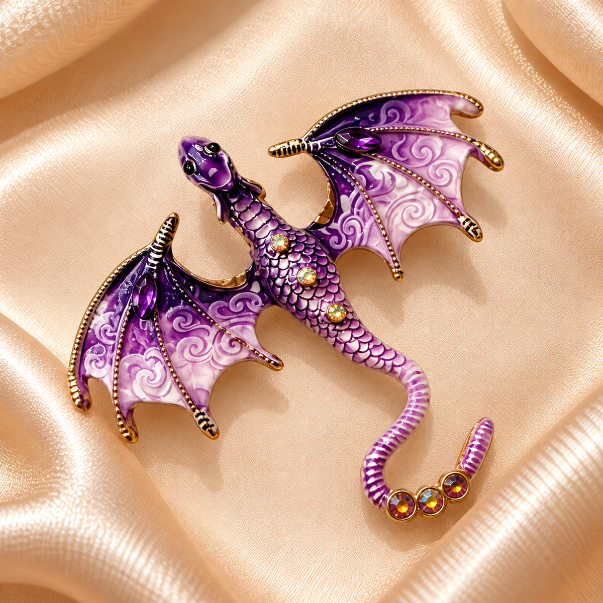 Broche dragon violet et mauve à ailes déployées, détails dorés et cristaux sur fond carré de satin champagne