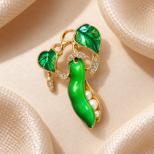 Broche haricot magique vert émeraude et doré avec perles et strass sur fond carré en satin champagne