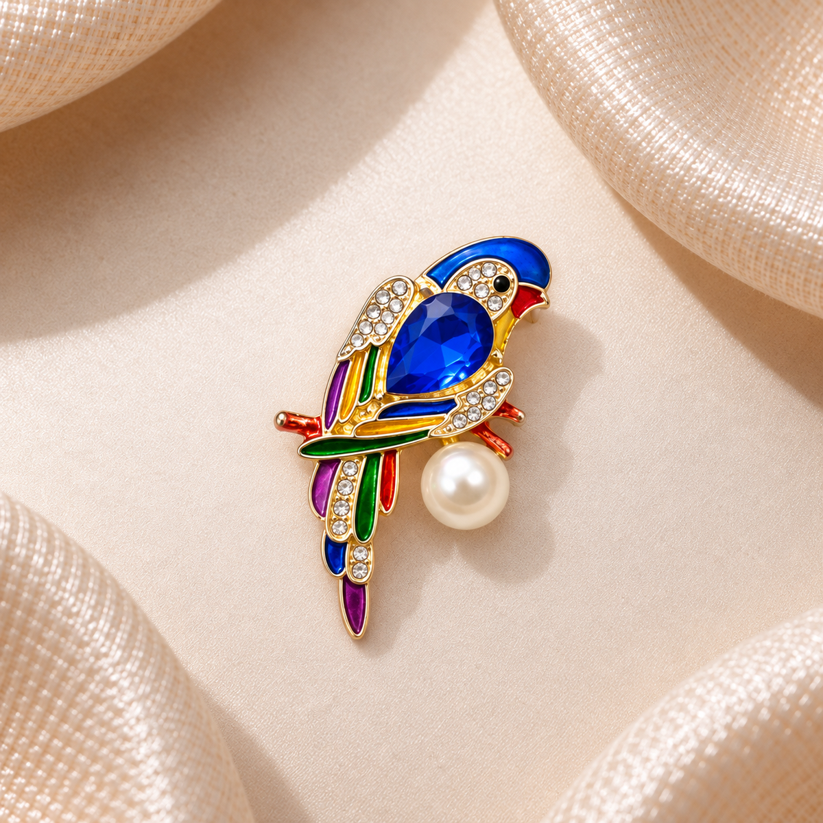 Broche perroquet bleu saphir multicolore avec strass dorés et perle blanche sur fond champagne satiné