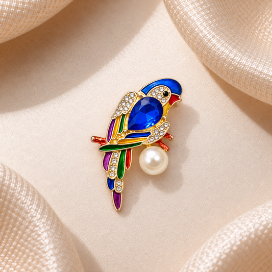 Broche perroquet bleu saphir multicolore avec strass dorés et perle blanche sur fond champagne satiné