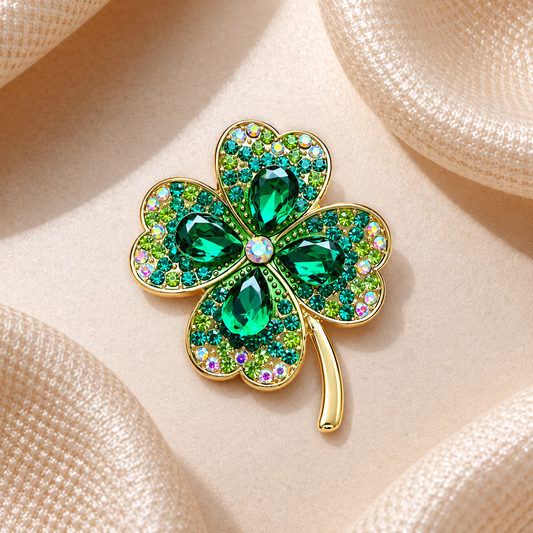 Broche trèfle à quatre feuilles dorée ornée de strass verts, turquoise et pierres émeraude sur fond carré champagne satiné
